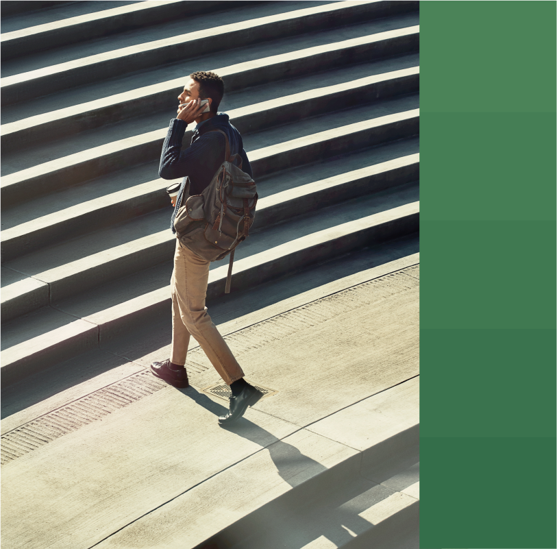 photo of a man in his 20s with a backpack walking up a set of stone stairs outside while talking on a phone.