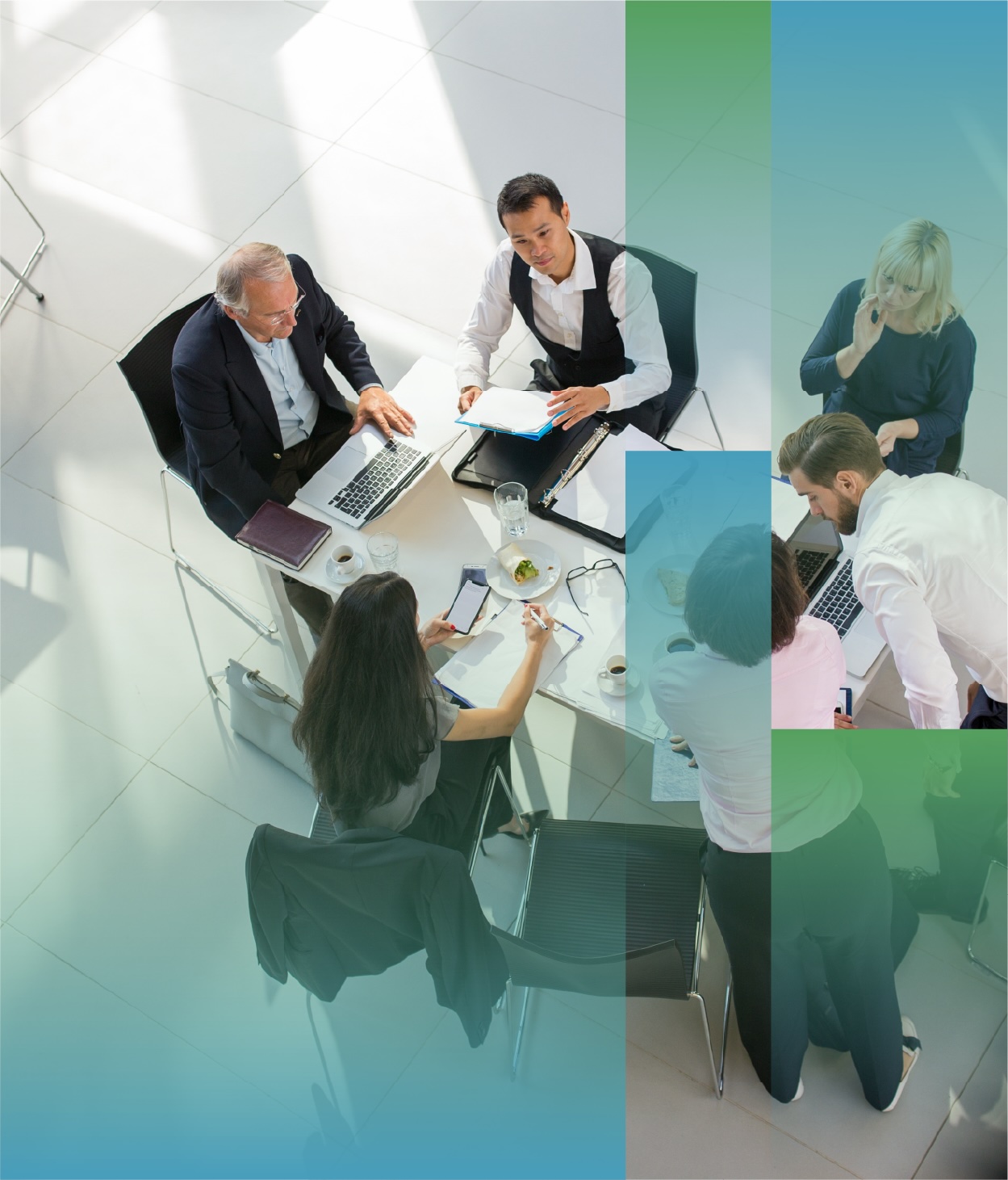 Overhead view of several people seated around a small round table in a bright office space, working with laptops, documents, notebooks, and coffee cups, with abstract blue and green graphic overlays partially framing the scene.