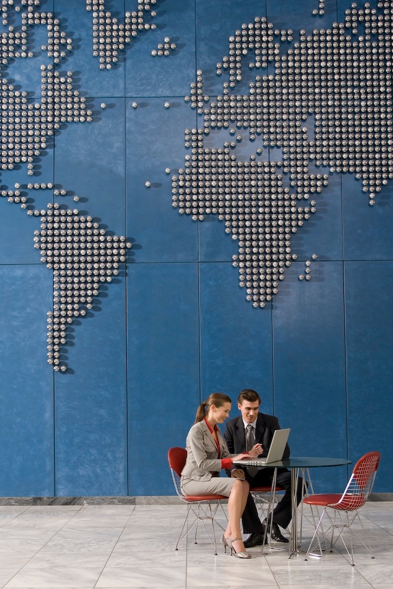 Business colleagues using laptop in office with world map on wall